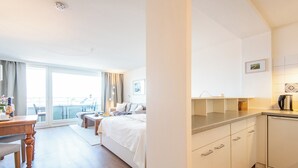 A modern hotel room with a bed, a dining table, a kitchen area, and a balcony with a view. - Hanseatenhaus Sea Nest 43 - Westerland (Westerland)