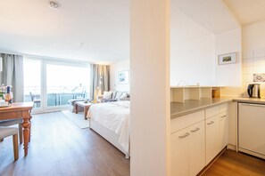 A modern hotel room with a bed, a dining table, a kitchen area, and a balcony with a view. - Hanseatenhaus Sea Nest 43 - Westerland (Westerland)