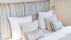 Ein Bett mit weißer Bettwäsche, gestreiften Kissen und einem Kopfteil mit einer Leuchte.