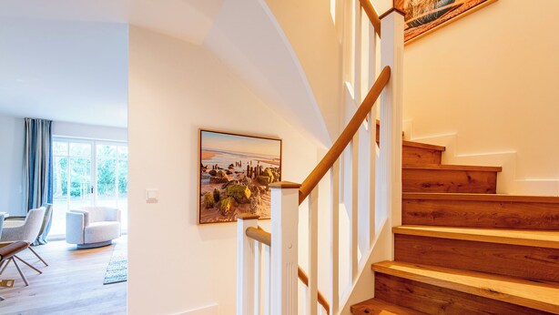 Eine Treppe mit Holzstufen und weißen Geländern, ein Essbereich mit Stühlen und einem Tisch sowie ein Gemälde an der Wand.