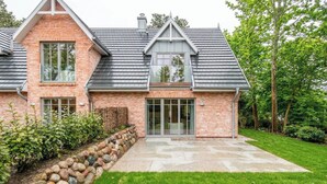 Ein zweistöckiges Haus mit Backsteinfassade, großen Fenstern und einem Steinweg zum Eingang.