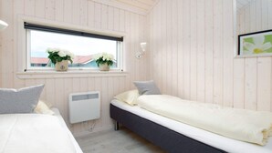 A room with two beds, a window with plants, a wall-mounted heater, and a mirror. - 4 Star Holiday Home in Grossenbrode (Grossenbrode)