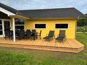 A yellow building with a wooden deck, black chairs, and a table. - 4 Star Holiday Home in Grossenbrode (Grossenbrode)