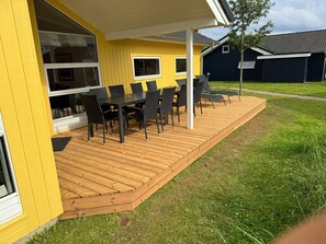 A yellow building with a wooden deck, outdoor seating, and a window. - 4 Star Holiday Home in Grossenbrode (Grossenbrode)
