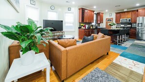 A living room with a brown sofa, a TV, and a plant. - Spacious & Cozy 4BR Boston Apt with view / Family Gathering - 90/2 (Boston)