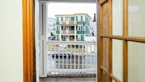 A view from a balcony with a wooden railing, a street with cars, and a multi-story building with a green facade. - Spacious & Cozy 4BR Boston Apt with view / Family Gathering - 90/2 (Boston)