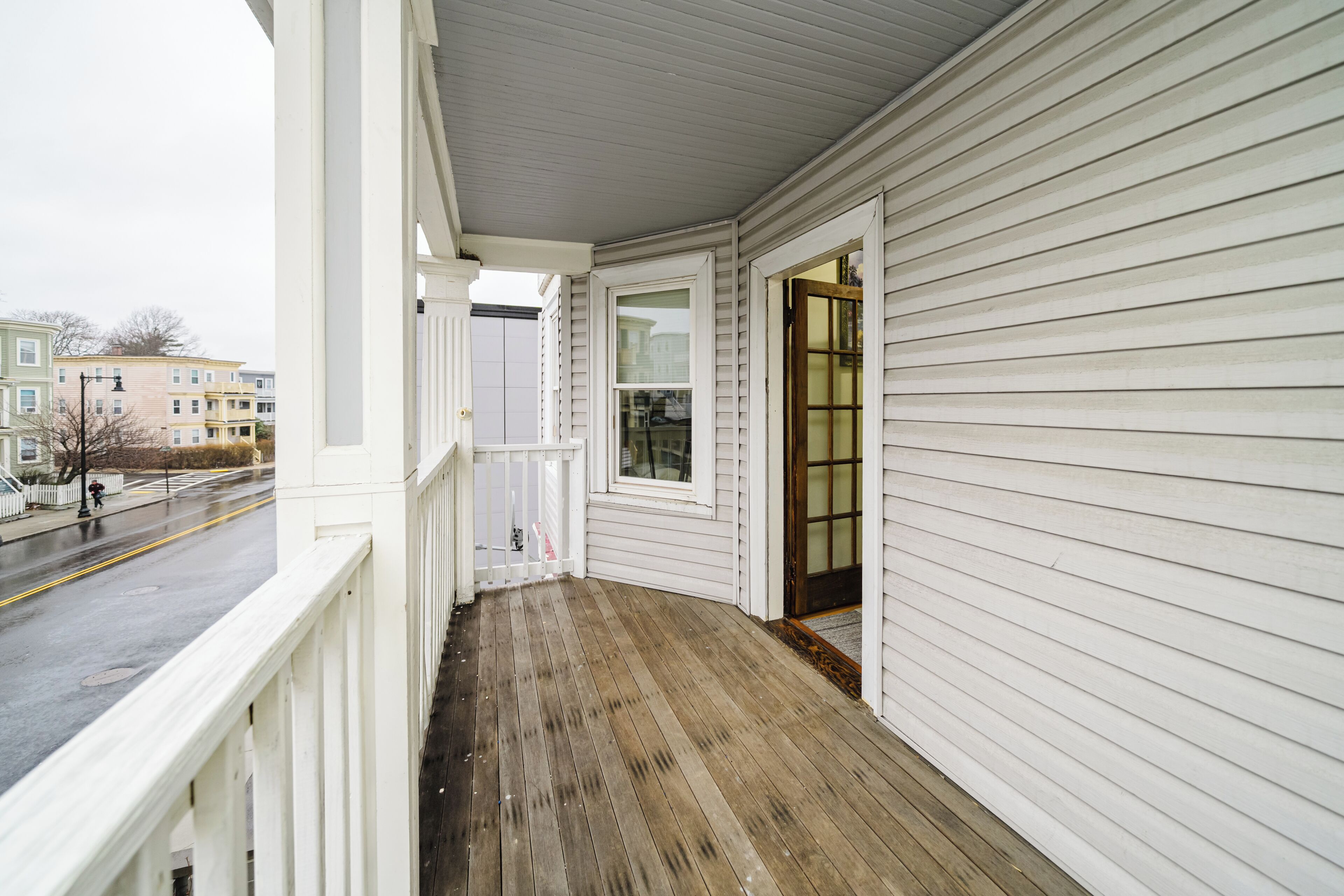 A covered porch with a wooden floor, white siding, and a view of the street.