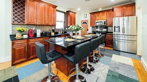 A modern kitchen with wooden cabinets, a central island with bar stools, stainless steel appliances, and a patterned rug. - Spacious & Cozy 4BR Boston Apt with view / Family Gathering - 90/2 (Boston)