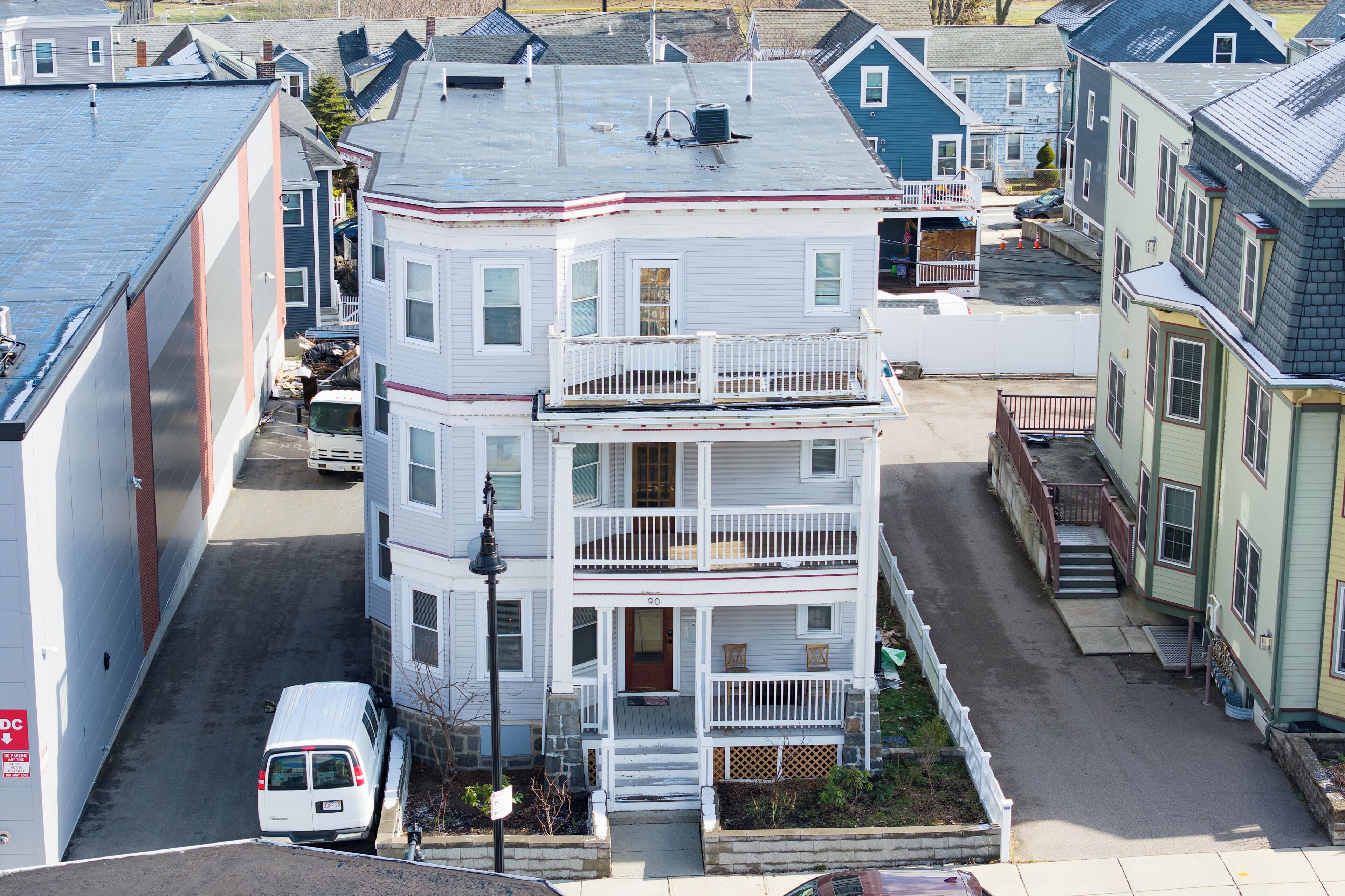 A multi-story residential building with a front porch, a visible garage door, and a street view.