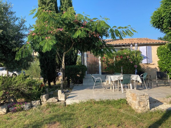 A patio area with outdoor seating, a stone wall, and a building with a tiled roof. - "L'Olivier"—air-conditioned house / 700 m² (Ruoms)