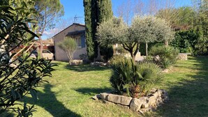 A garden with a stone wall, a palm tree, and a building with a sloped roof. - "L'Olivier" air-conditioned house / 700 m2 (Ruoms)