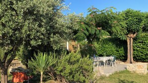 A garden with various plants and trees, a stone wall, and a table with chairs. - "L'Olivier" air-conditioned house / 700 m2 (Ruoms)