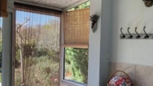 A room with a sliding glass door leading to a garden, a small shelf with a basket, and a wall-mounted light fixture. - "L'Olivier" air-conditioned house / 700 m2 (Ruoms)