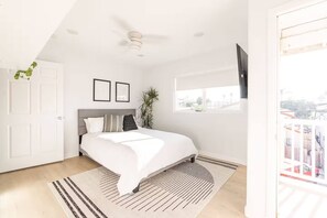 A bedroom with a bed, a ceiling fan, a window with a view, and a door. - Ocean Beach Compound, Walk to Beach, Sleeps 19, Driveway and 3 parking garages (San Diego)