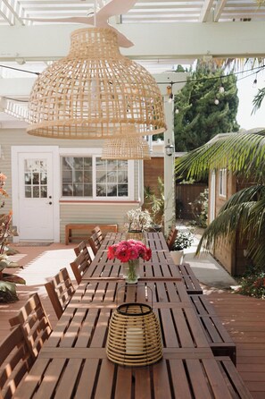 Eine Holzterrasse im Freien mit Esstisch, Stühlen, einer Korlampen und einem Blumenstrauß.
