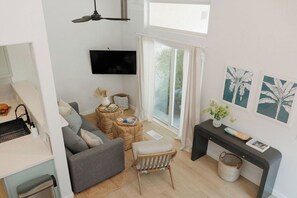 A modern living room with a grey sofa, a wooden chair, a coffee table, and a flat-screen TV mounted on the wall. - Ocean Beach Compound, Walk to Beach, Sleeps 19, Driveway and 3 parking garages (San Diego)