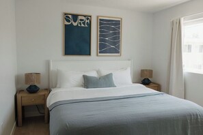 A bedroom with a bed, two nightstands, a window with curtains, and two wall art pieces. - Ocean Beach Compound, Walk to Beach, Sleeps 19, Driveway and 3 parking garages (San Diego)