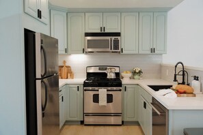 A modern kitchen with stainless steel appliances, light green cabinets, and a herringbone-patterned backsplash. - Ocean Beach Compound, Walk to Beach, Sleeps 19, Driveway and 3 parking garages (San Diego)