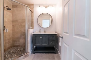 A bathroom with a shower, a vanity with a mirror, and a door. - Ocean Beach Compound, Walk to Beach, Sleeps 19, Driveway and 3 parking garages (San Diego)