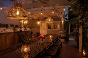 Ein Außenbereich mit Essbereich, Holztische und -bänke, Lichterketten und hängende Lampen.