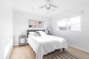A bedroom with a bed, a nightstand, a lamp, a ceiling fan, and a window. - Ocean Beach Compound, Walk to Beach, Sleeps 19, Driveway and 3 parking garages (San Diego)