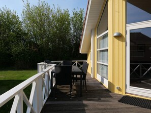 A wooden deck with a table and chairs, a white railing, and a yellow building with large windows. - 4 Star Holiday Home in Grossenbrode (Grossenbrode)