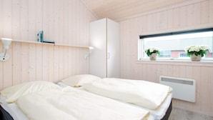Quarto com duas camas, janela com plantas, radiador e guarda-roupa branco.