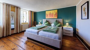 Ein Doppelbett mit Kopfteil, zwei Nachttische mit Lampen, ein Fenster mit Vorhängen und ein Bild an der Wand.