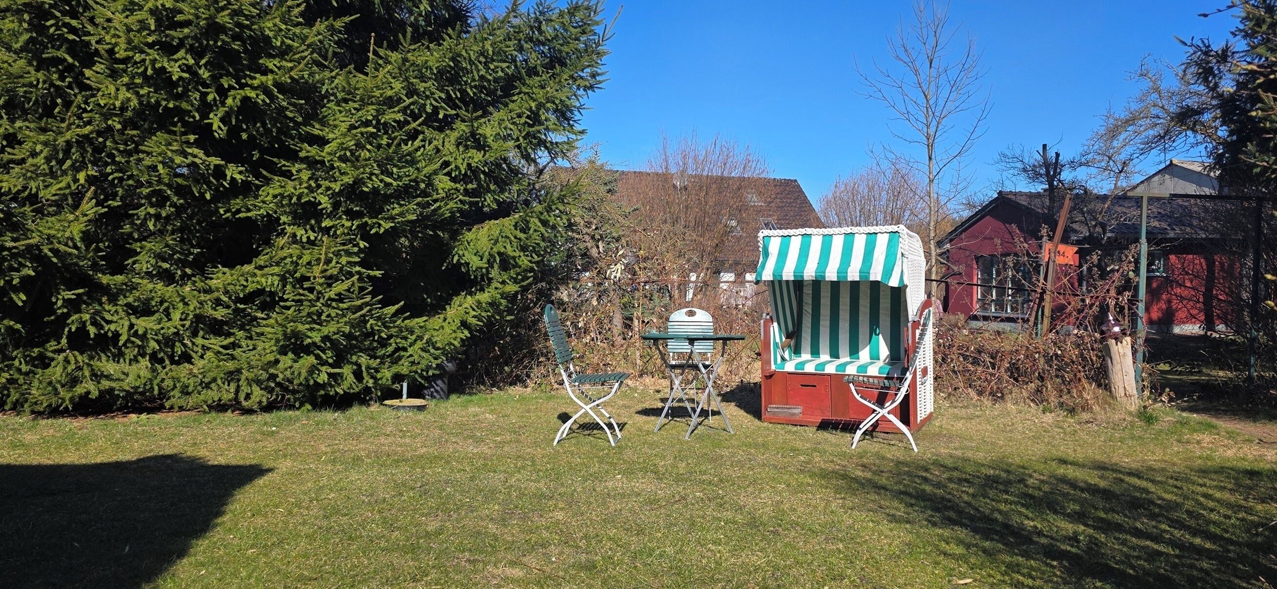 A grassy outdoor area with a green and white striped beach chair, a small table, and a metal chair.