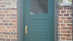 Una puerta verde con un ventanal, un timbre de latón y un escalón que conduce a la entrada.