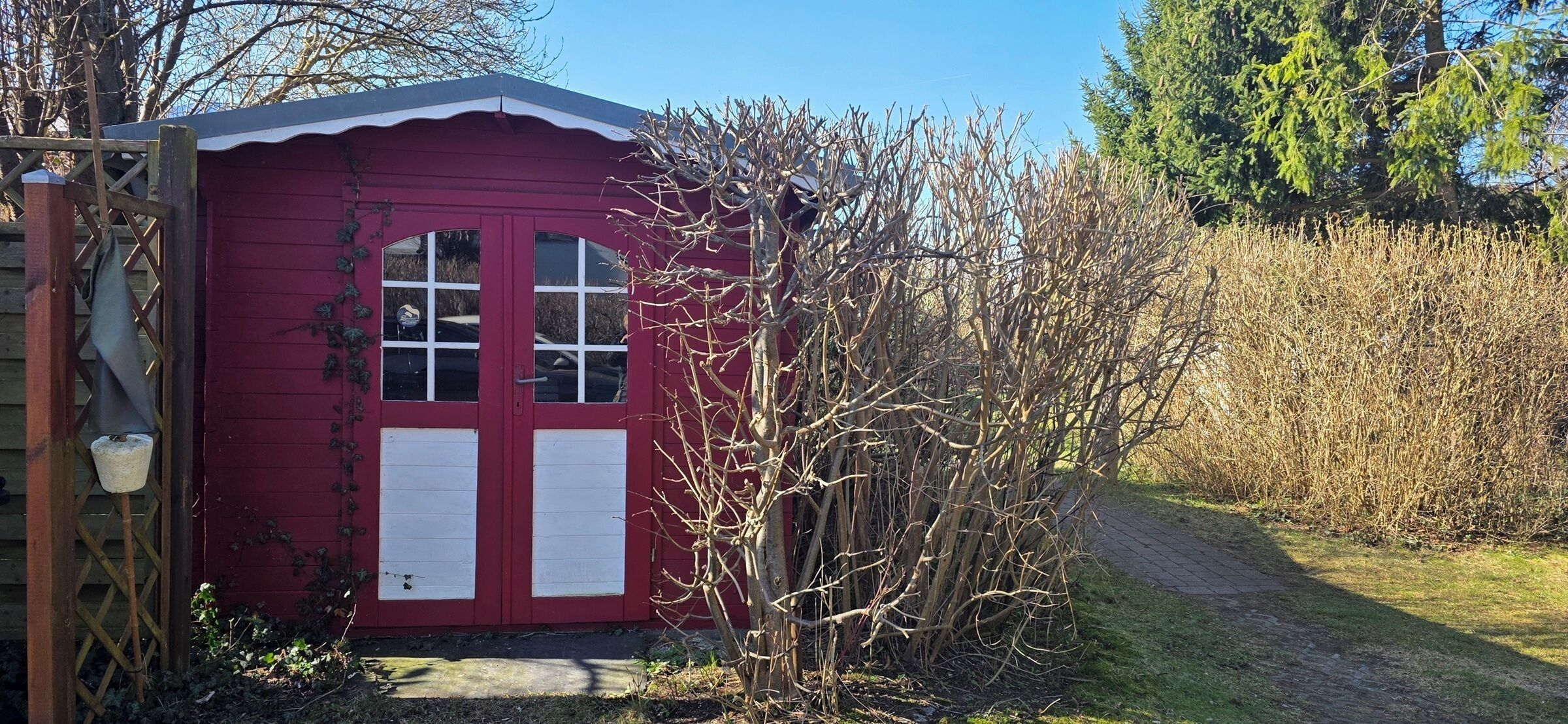 Una rimessa rossa con una porta e finestre, circondata da alberi spogli e un sentiero.