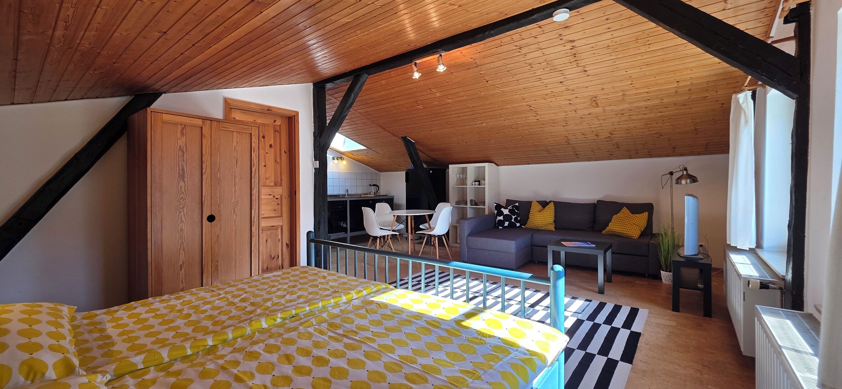 A bedroom with a bed, a balcony, a kitchenette, and a living area with a sofa and chairs.