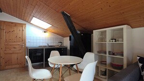 Una cocina compacta con techo de madera, un área de comedor con sillas blancas y un armario blanco con vajilla.