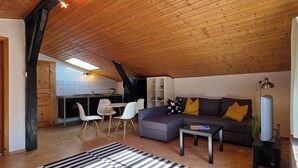 Un espacio habitable tipo loft con techo de madera, un sofá, una mesa de comedor y una zona de cocina.