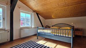 Un dormitorio con techo inclinado, una cama, una mesita de noche y una ventana.