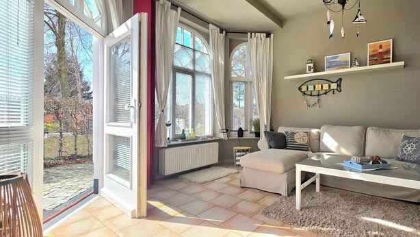 Un salon avec un canapé, une table basse et une porte ouverte donnant sur un jardin.