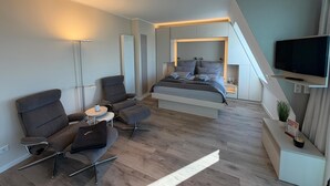 A modern bedroom with a bed, a TV, a desk, and a chair. - Anna Düne 3-41 - Dream location in the Aparthotel Anna Düne with a view of the Wadden Sea (Wangerooge)