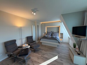 Ein modernes Schlafzimmer mit Bett, Fernseher, Schreibtisch und Stuhl.
