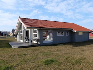 A single-story house with a red-tiled roof, a covered patio with outdoor furniture, and a large sliding glass door. - 4 Star Holiday Home in Grossenbrode (Grossenbrode)