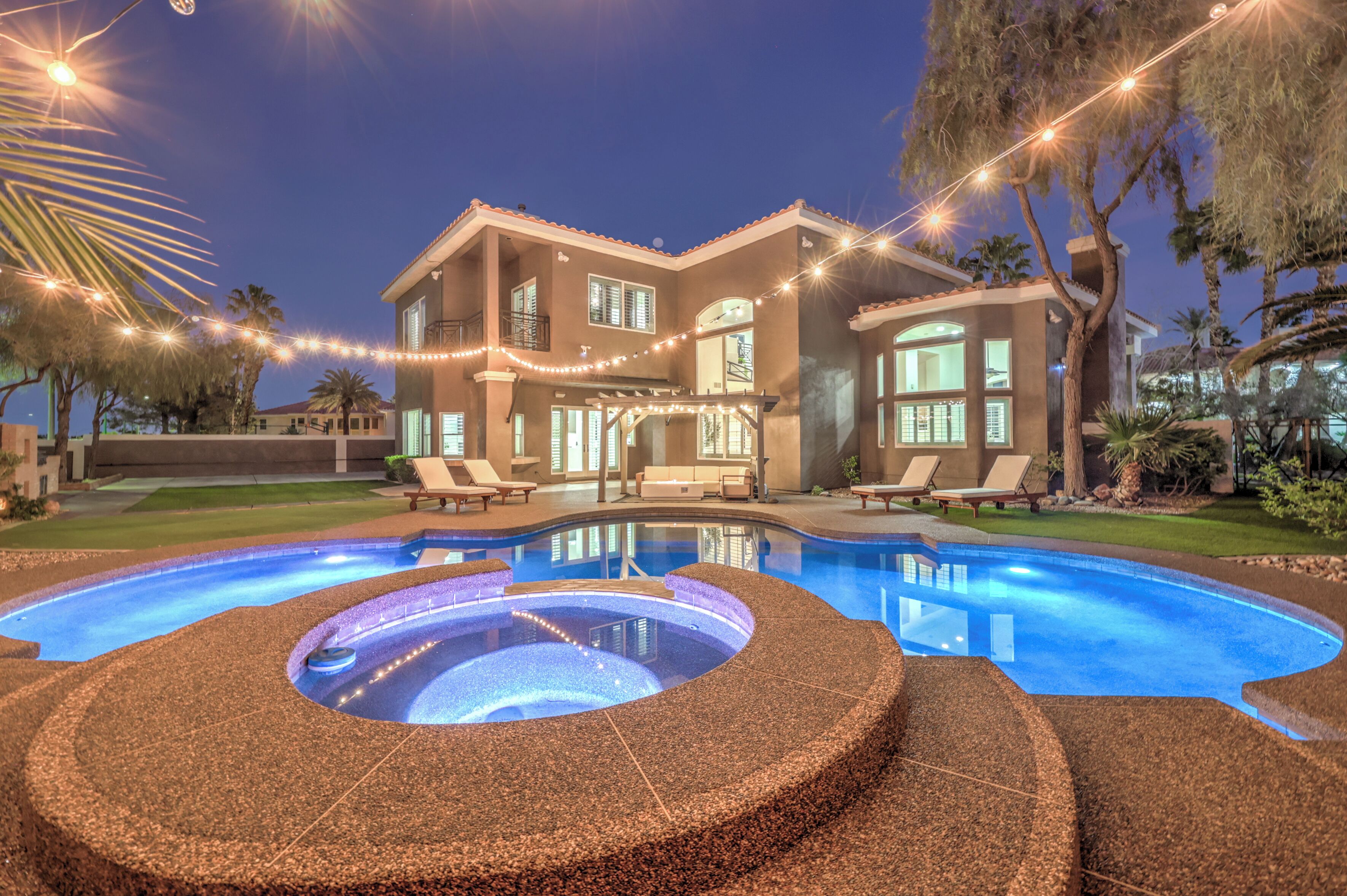 Ein zweistöckiges Haus mit Swimmingpool, Sitzgelegenheiten im Freien und Lichterketten.