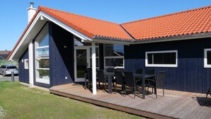 Uma casa moderna com uma grande porta de vidro, um alpendre coberto com mobiliário de exterior e um telhado de telhas vermelhas.