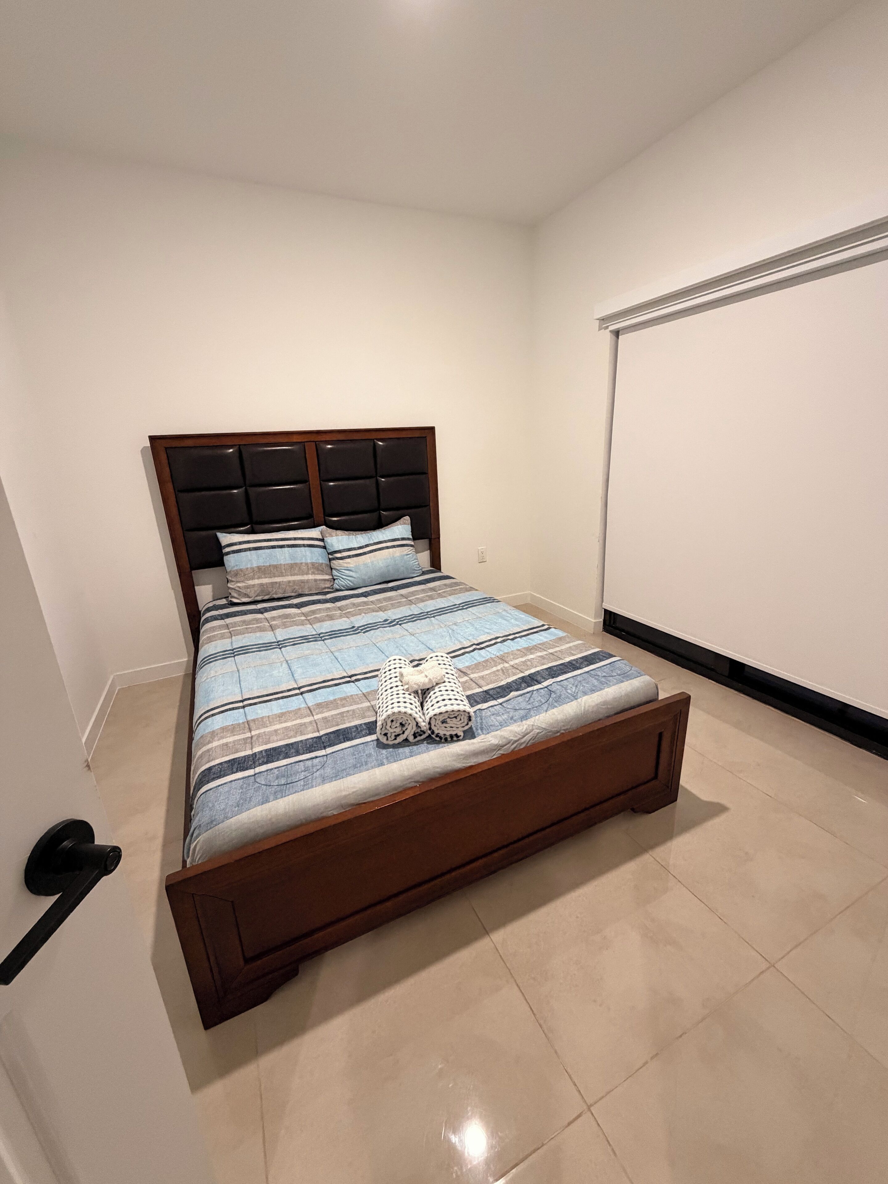Un dormitori amb un llit, una capçalera, una porta i una pantalla projectora penjada a la paret.