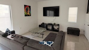 A modern living room with a sectional sofa, a glass coffee table, a flat-screen TV, and a fireplace. - Spacious 4-bedroom house in wonderful Florida City with AC (Florida City)