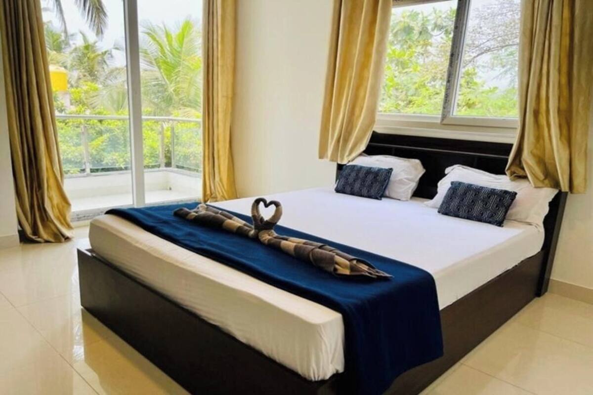 Ein Hotelzimmer mit einem großen Bett, Blick auf Grünfläche und Vorhängen an den Fenstern.