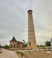 A tall, cylindrical tower with a dome-shaped structure at its base, surrounded by a landscaped area with pathways and sparse vegetation.