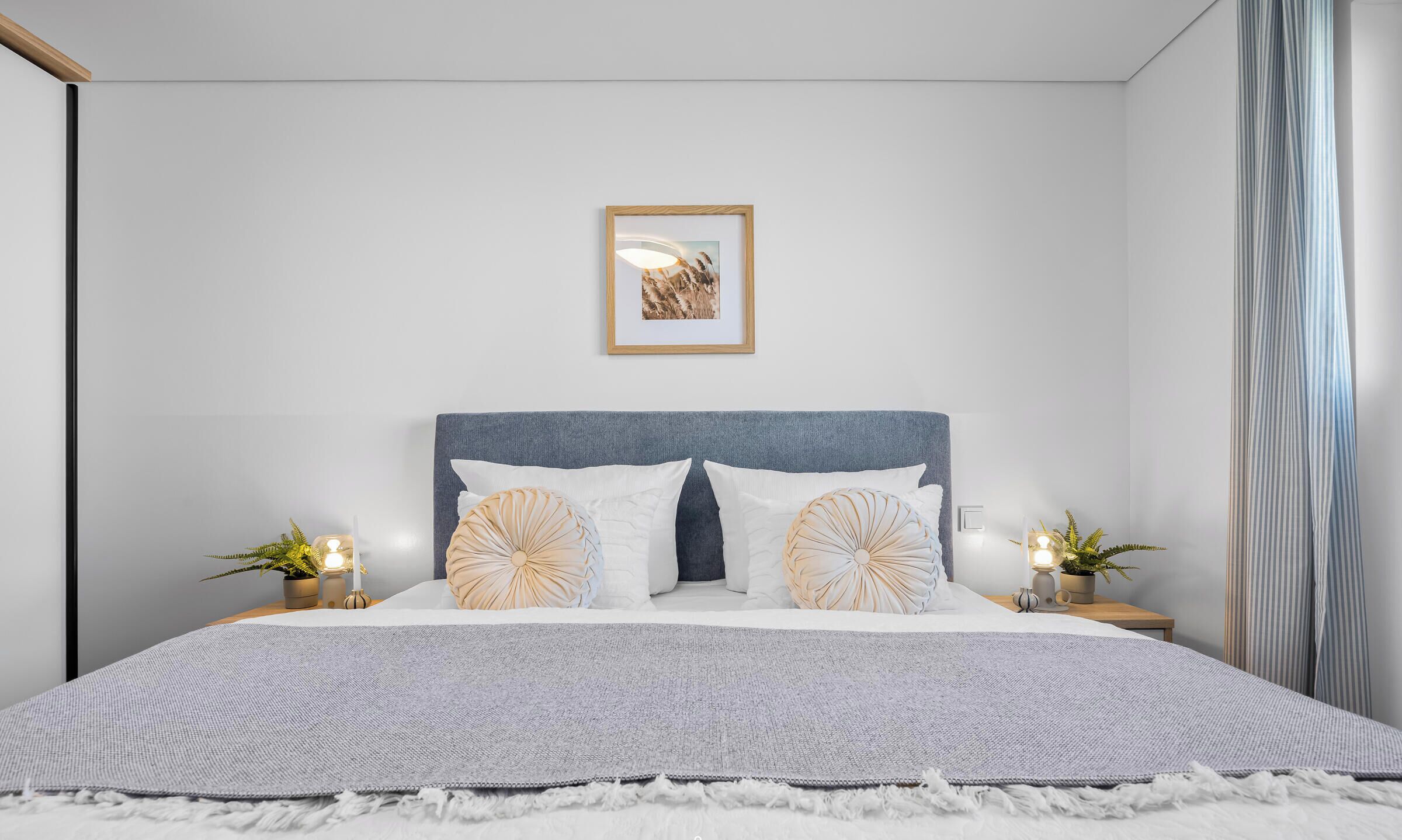 Quarto com cama, um quadro na parede e duas mesas de cabeceira com velas.