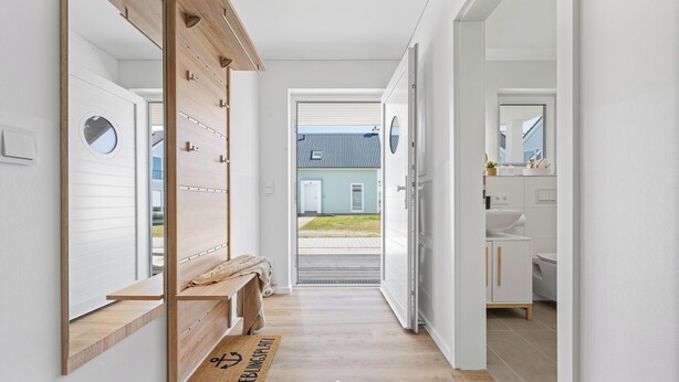 En hall med en träbänk, en dörr med ett fönster och utsikt över ett hus.