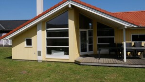 Una casa de un piso con techo de tejas rojas, grandes ventanales de vidrio y una terraza de madera.