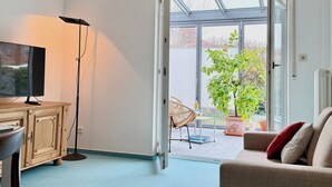 Una habitación con televisión, lámpara de pie, sofá, sillón y un ventanal con vista a la vegetación.