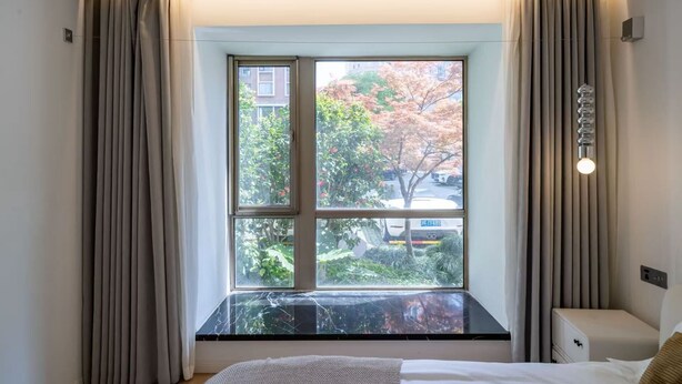 Une chambre d’hôtel avec une grande fenêtre, un lit, une table de chevet et une lampe.